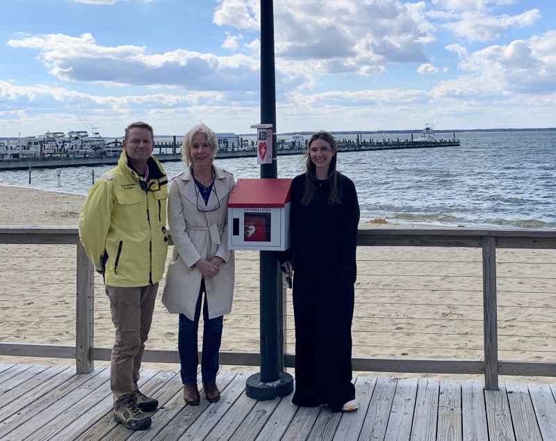 Laura Ashby, middle, stands next to the AED she recently donated to the Town of Dewey Beach that was installed on the public baywalk at Hyatt Place Dewey Beach. Ashby stands between Dewey Beach Town Manager Bill Zolper, left, and Alex Davis from Cardio Partners. SUBMITTED PHOTO